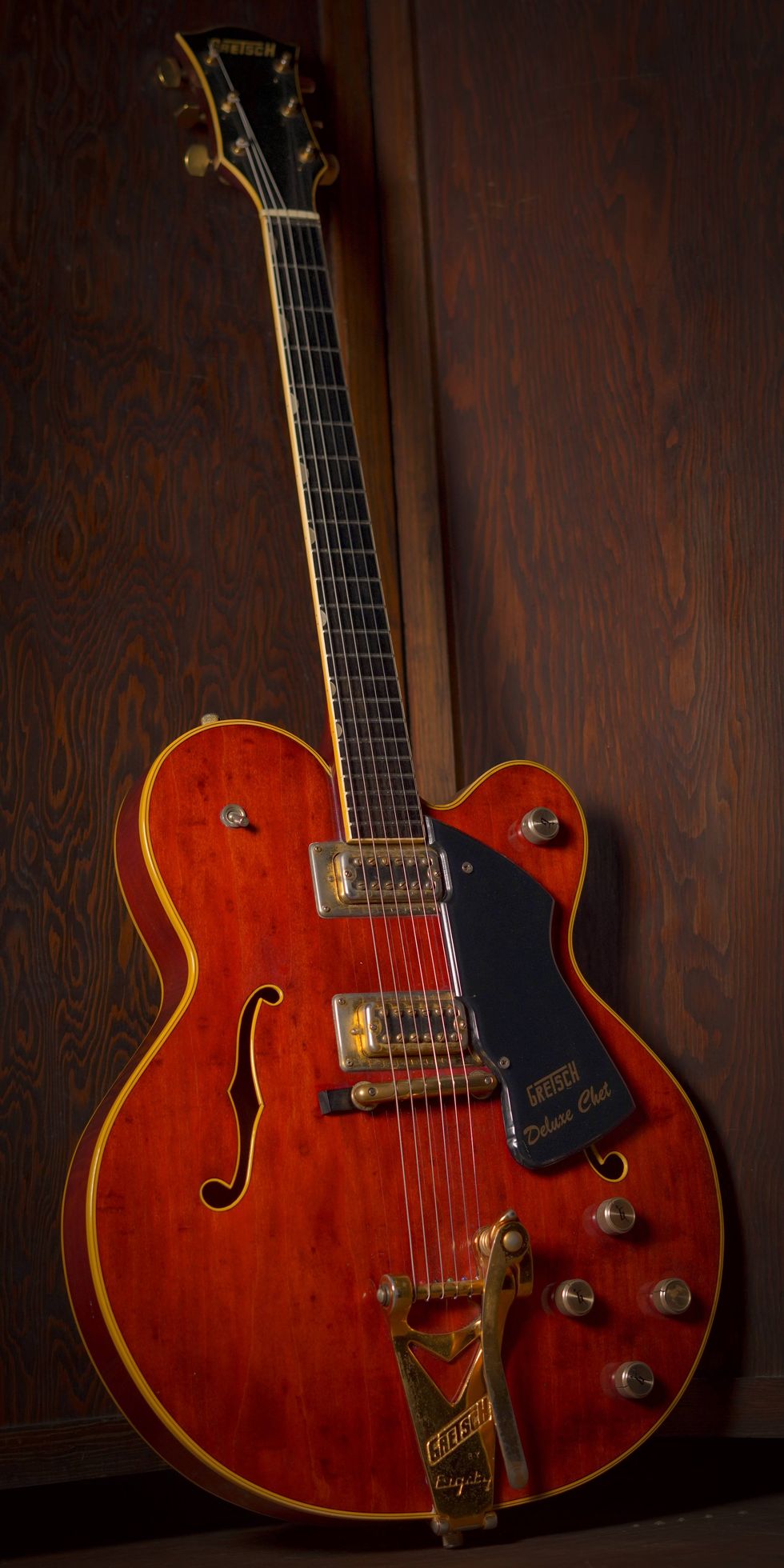 A vintage Gretsch guitar with a rich wooden finish against a dark wood background.