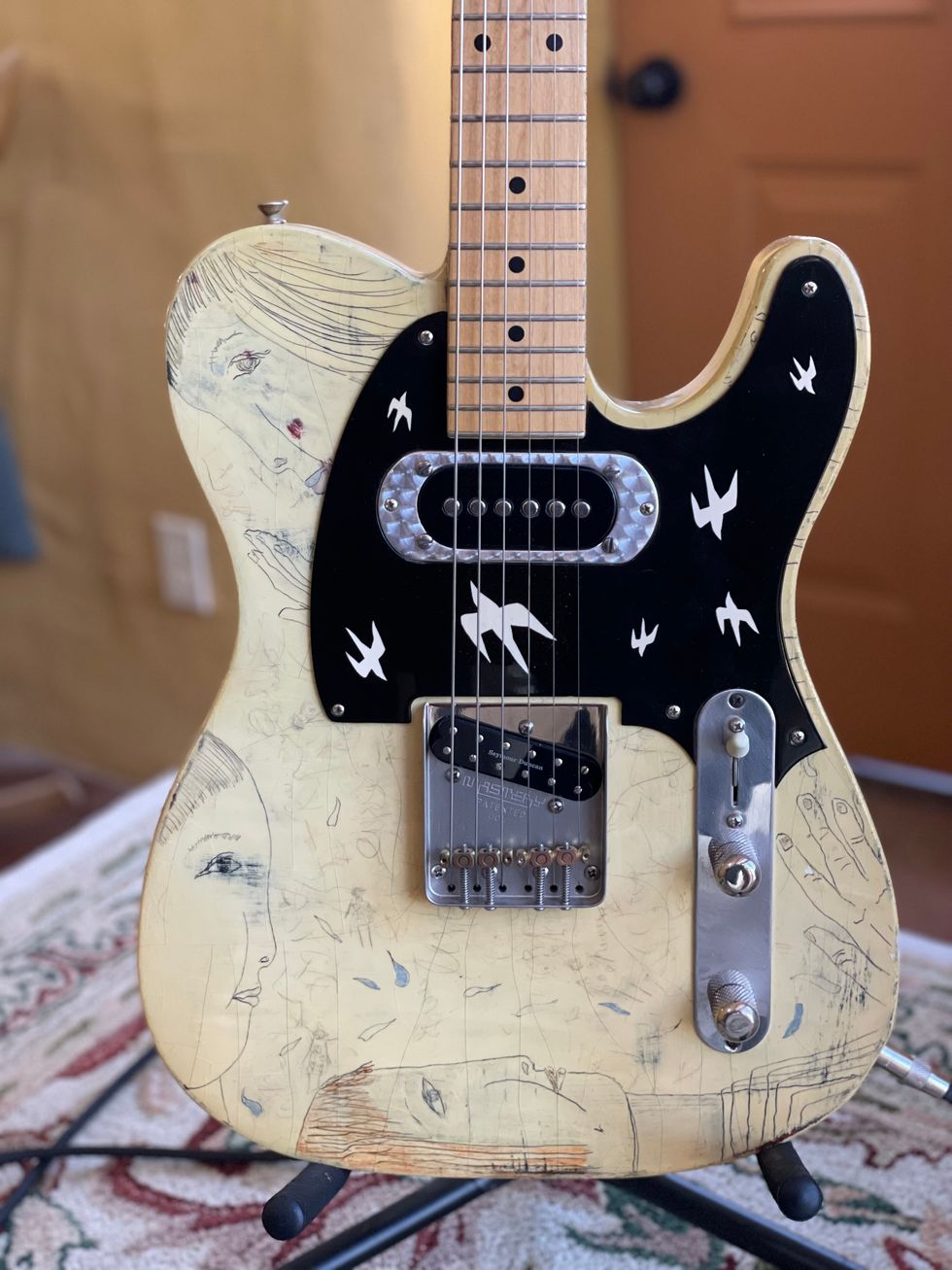 A vintage guitar with unique artwork featuring faces and birds on its body.