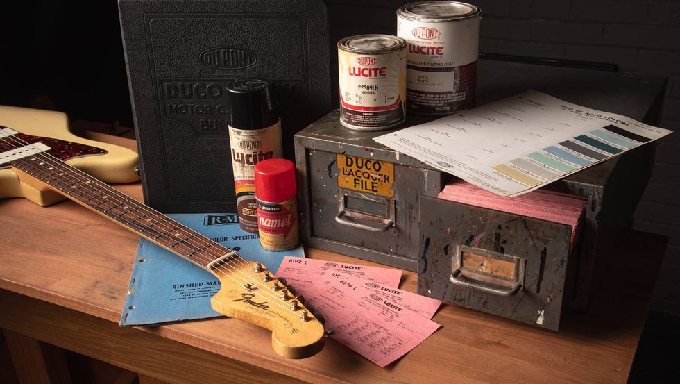 A vintage workspace with a guitar, paint cans, color samples, and reference materials.