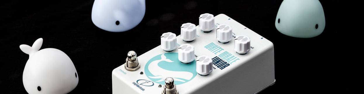A white effects pedal with knobs, surrounded by small whale toys and a battery pack.