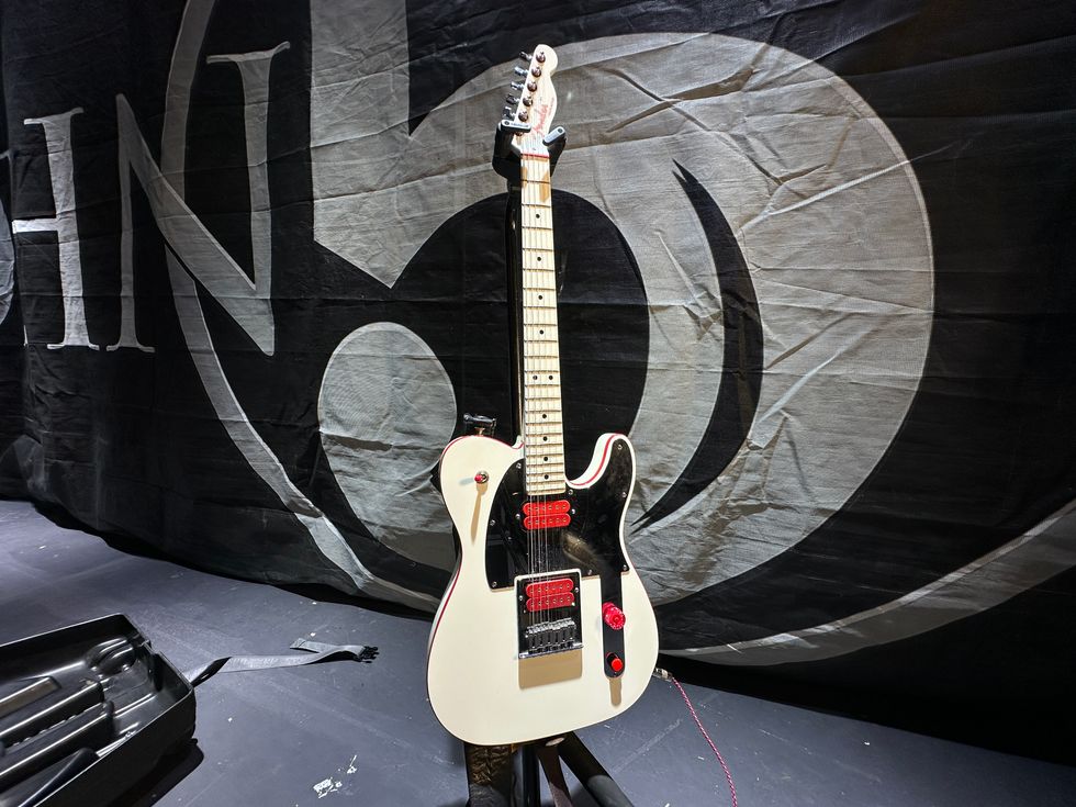 A white electric guitar with unique controls, set against a dark fabric backdrop.