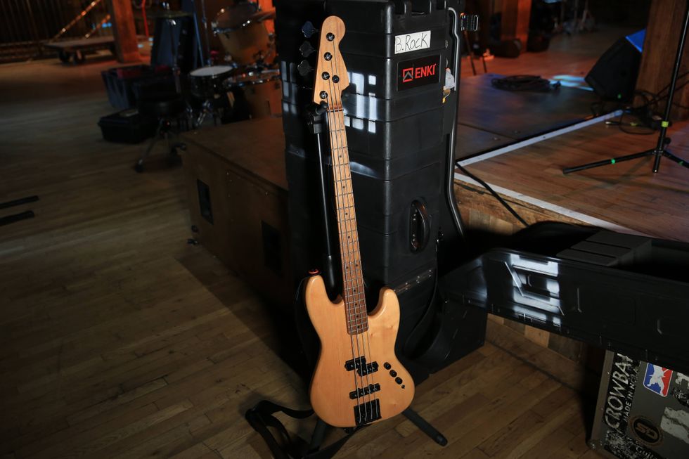A wooden bass guitar leans against a black amplifier on a wooden stage.