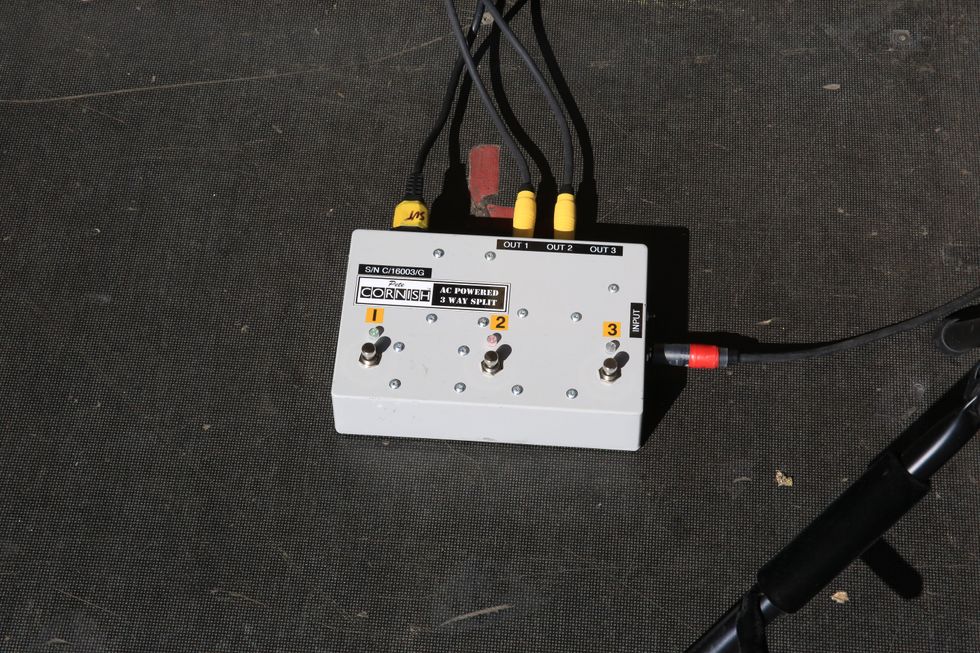 AC power splitter with three outputs and various cables on a dark surface.