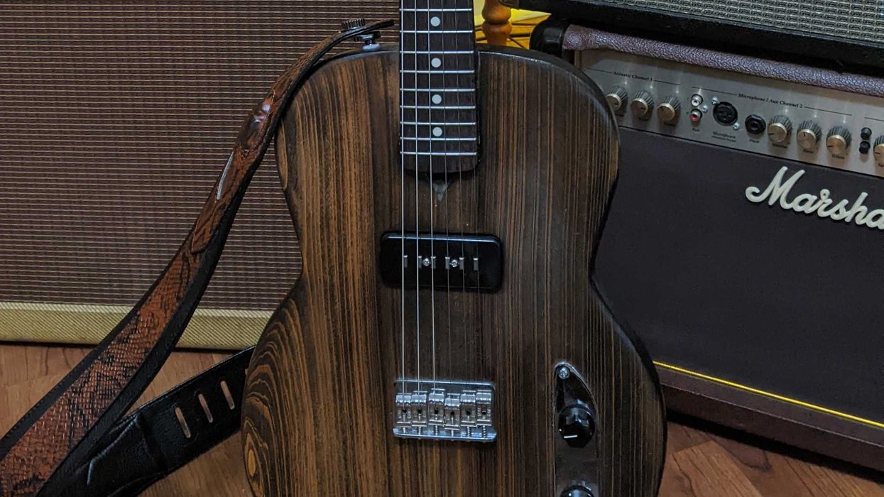 Acoustic guitar with a wooden finish, resting on a stand near amplifiers and photo frames.