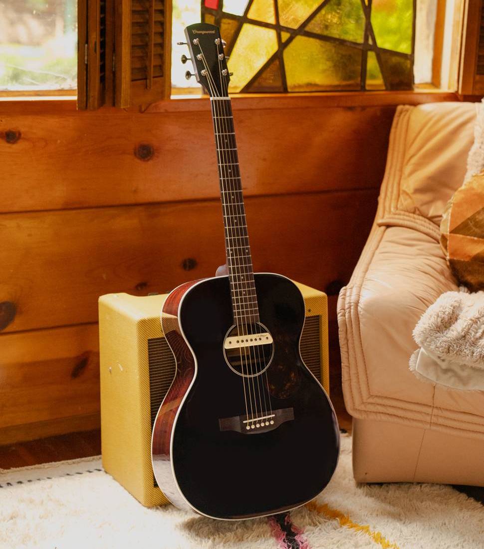 An acoustic guitar rests against a yellow amplifier in a cozy, sunlit room.