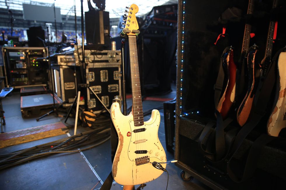 An old, distressed electric guitar stands among music equipment on stage.