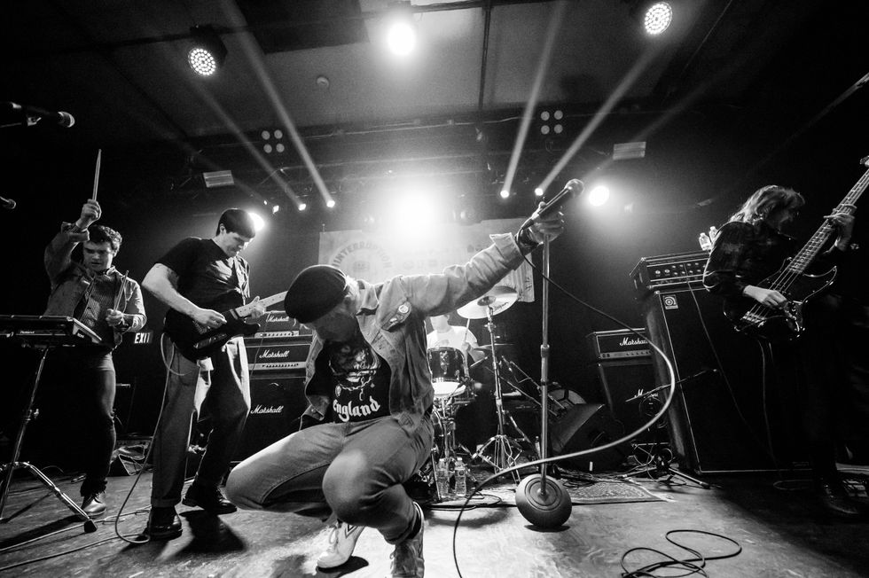 Band performing energetically on stage with instruments under dramatic lighting.