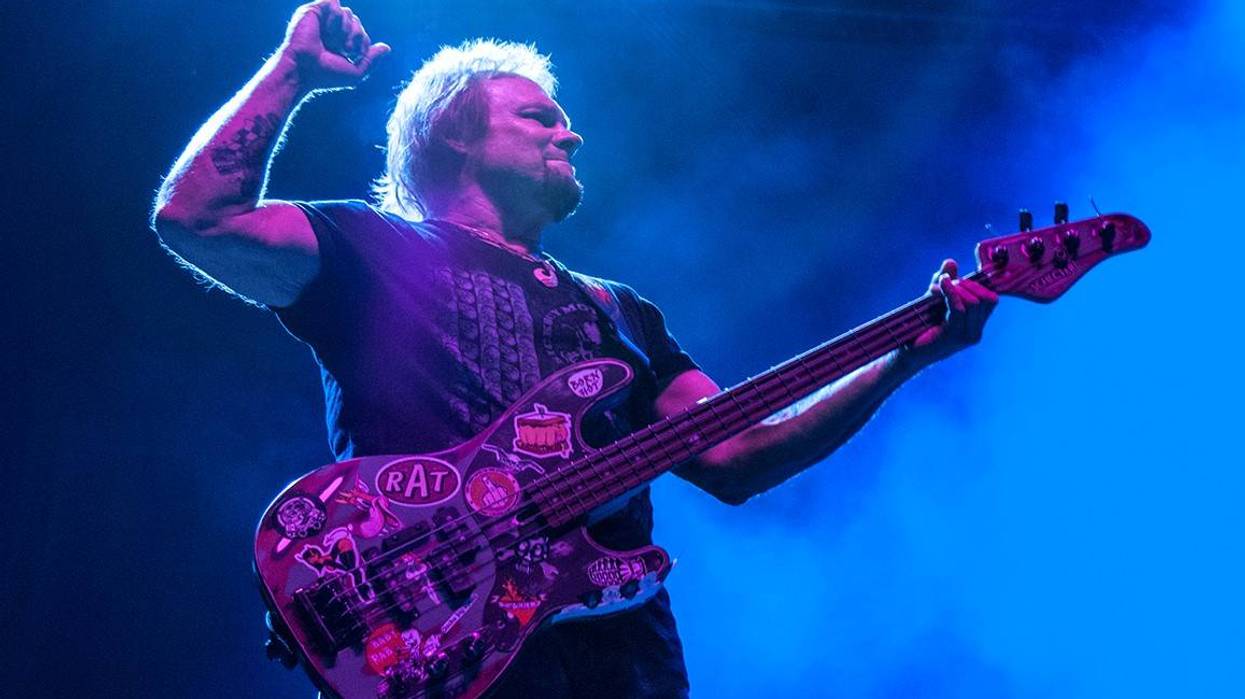 Bassist performing on stage, striking a confident pose amid vibrant blue lighting.