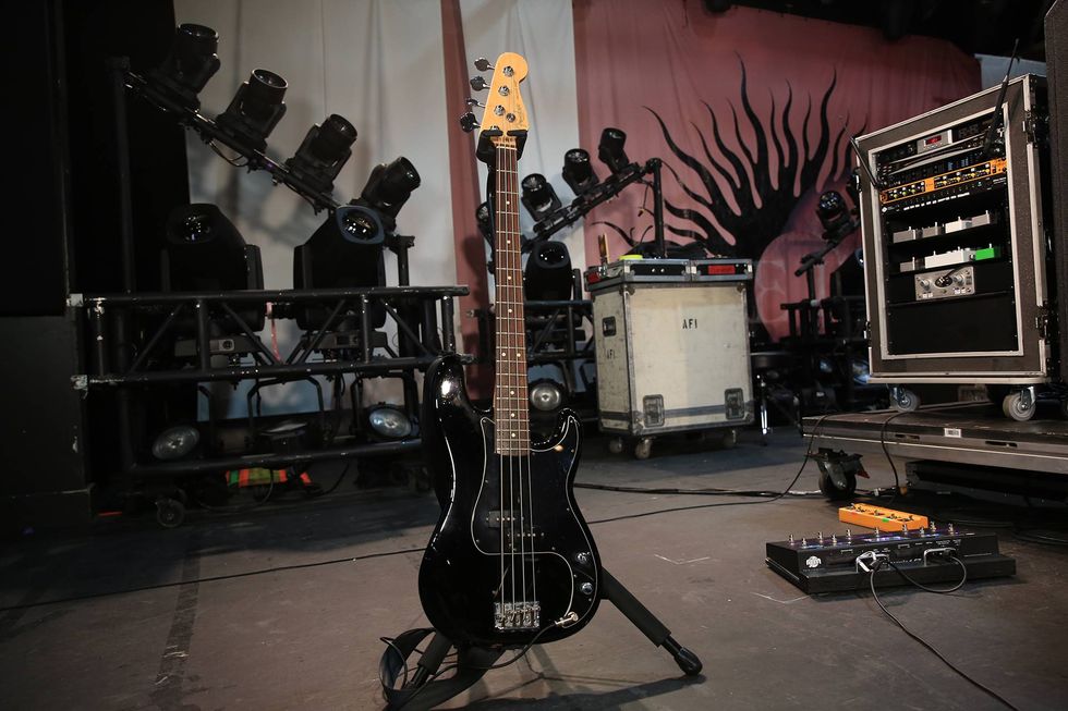 Black bass guitar on stage with lighting equipment and amplifiers in the background.