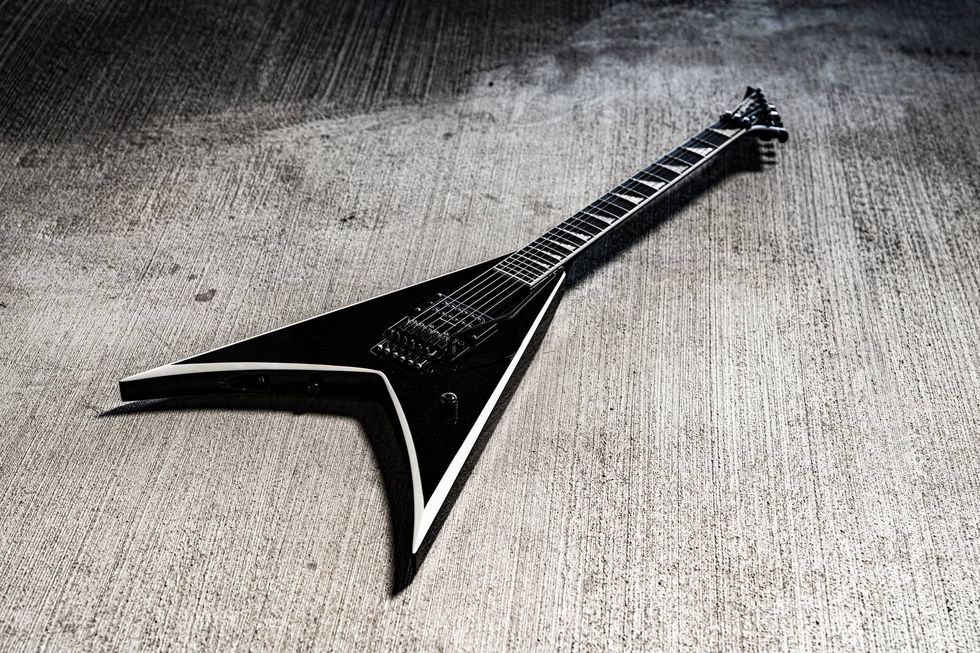 Black electric guitar with a sharp, angular design placed on a textured gray surface.