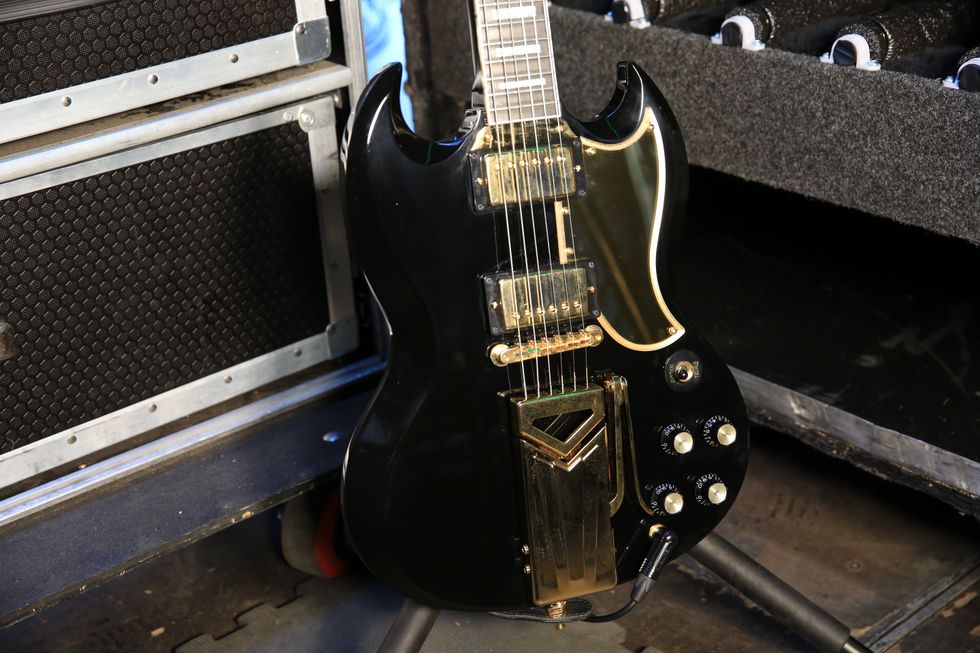 Black electric guitar with gold accents, leaning against equipment cases backstage.