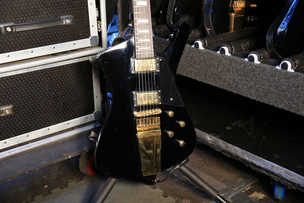 Black electric guitar with gold accents, leaning against equipment cases.