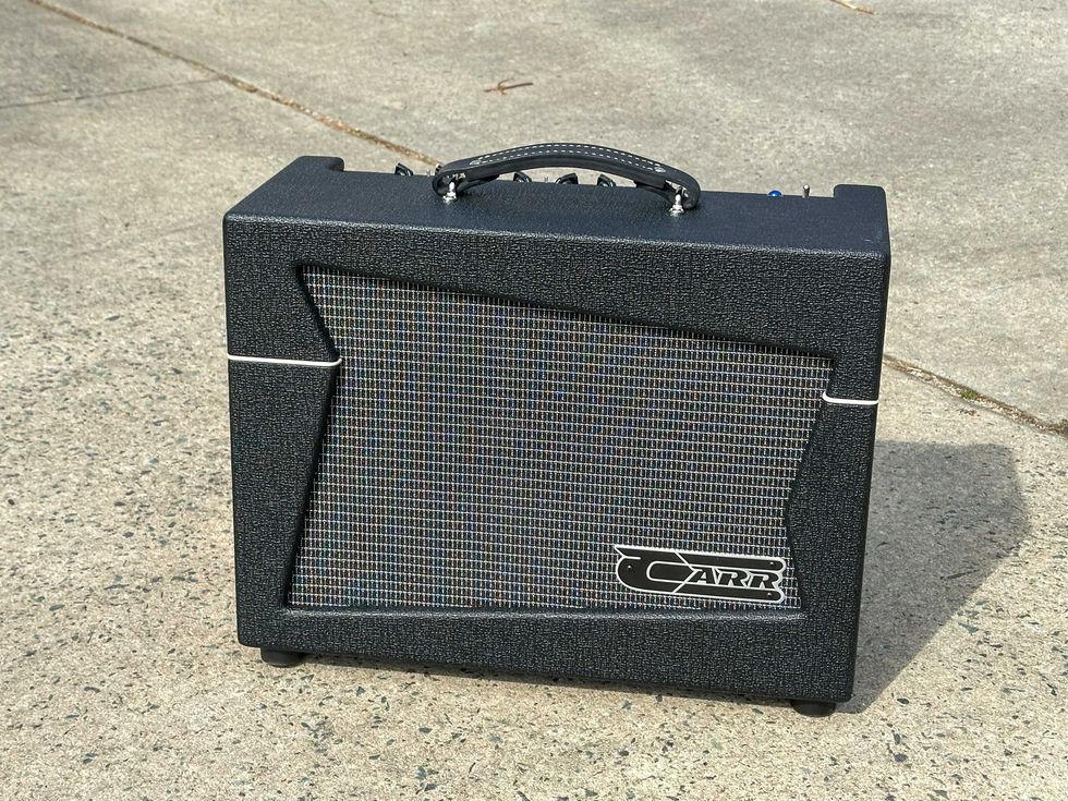 Black guitar amplifier with textured finish and speaker grille, resting on concrete.
