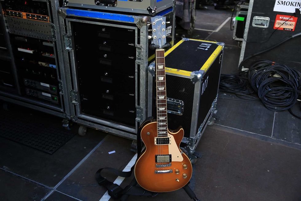 Brown electric guitar leaning against equipment cases on a stage.