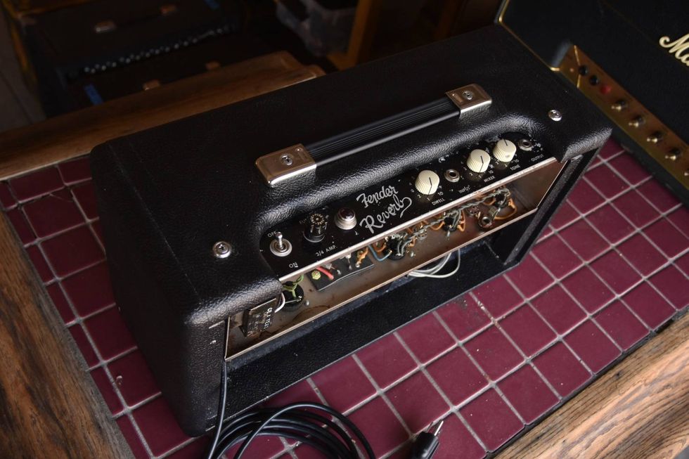 Close-up of a black Fender Reverb guitar amplifier on a tiled surface with visible knobs and wiring.