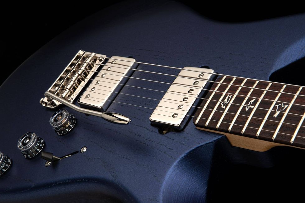 Close-up of a blue electric guitar showing metallic pickups and control knobs.