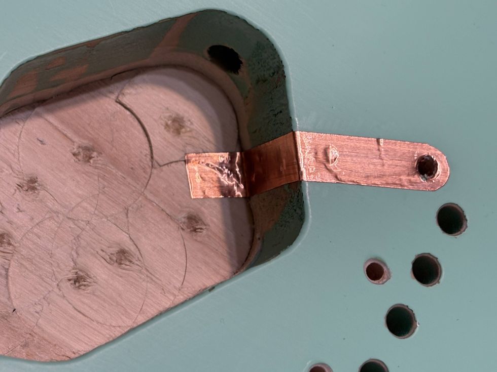 Close-up of a copper strip attached to a wooden surface with circular impressions.