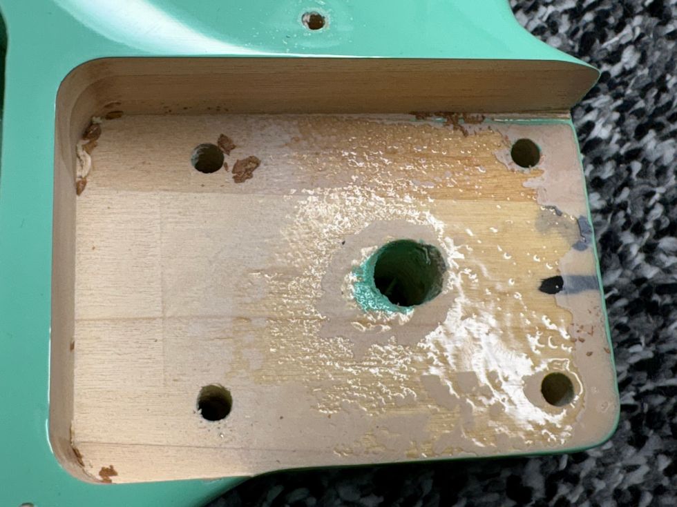 Close-up of a damaged guitar body section with exposed wood and drilling holes.