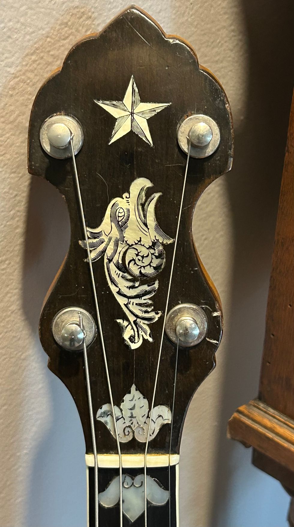 Close-up of a decorative banjo headstock with an inlaid star and bird design.