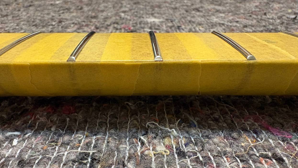 Close-up of a guitar fretboard covered with tape, resting on textured fabric.