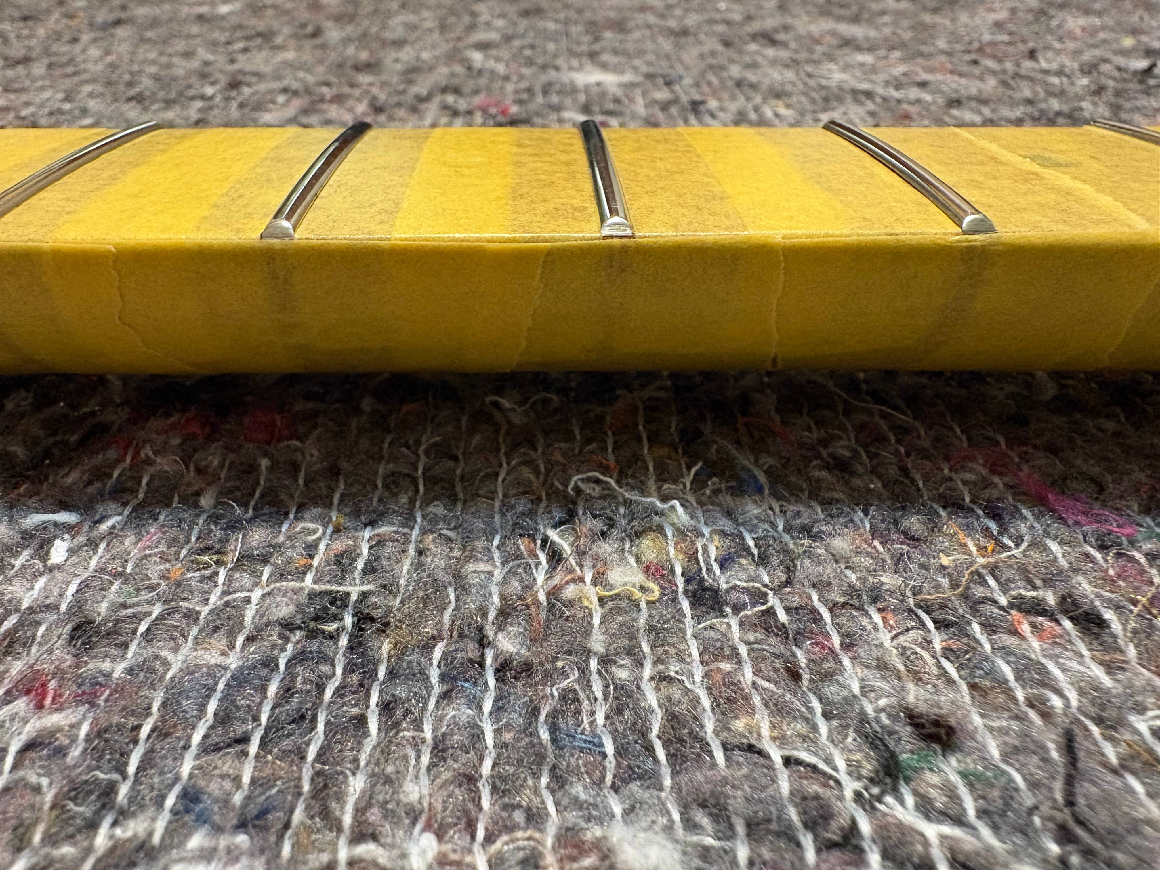 Close-up of a guitar fretboard covered with tape, resting on textured fabric.