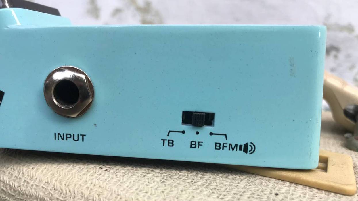 Close-up of a light blue audio device showing input jack and toggle switch settings: TB, BF, BFM.
