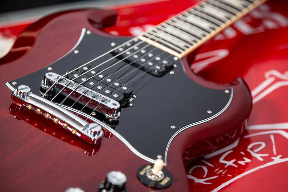 Close-up of a red electric guitar with a black pickguard and chrome hardware.