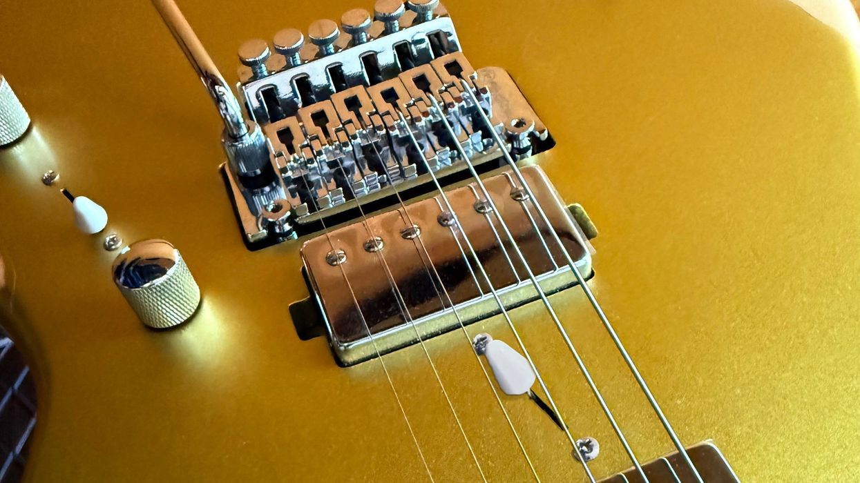 Close-up of a shiny gold electric guitar's bridge and strings.