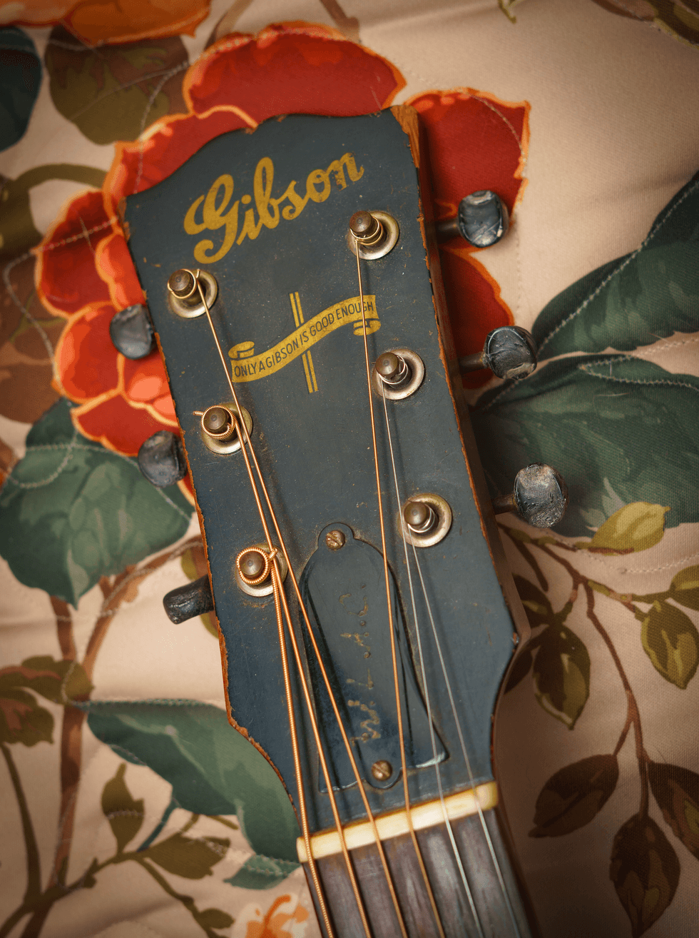 Close-up of a vintage Gibson guitar headstock on a floral fabric background.