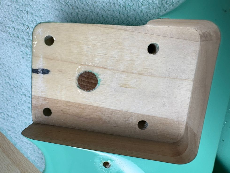 Close-up of a wooden guitar neck plate with holes and a light green guitar body.