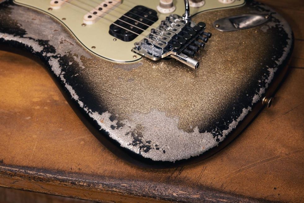Close-up of a worn electric guitar with a distressed finish on a wooden surface.
