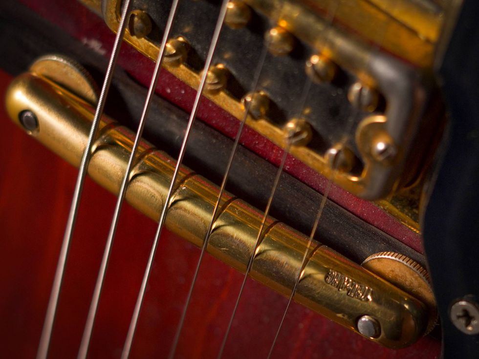 Close-up of guitar strings and bridge with brass and metal components. Rich wood background.