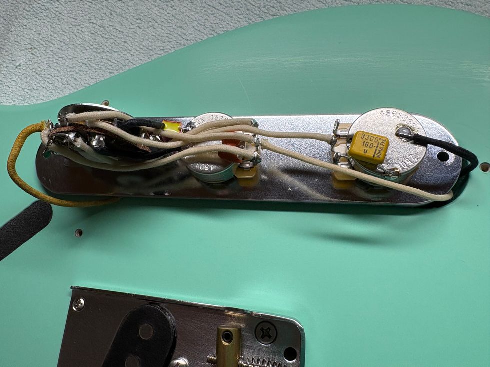 Close-up of guitar wiring, pots, and capacitor on a mint green guitar body.