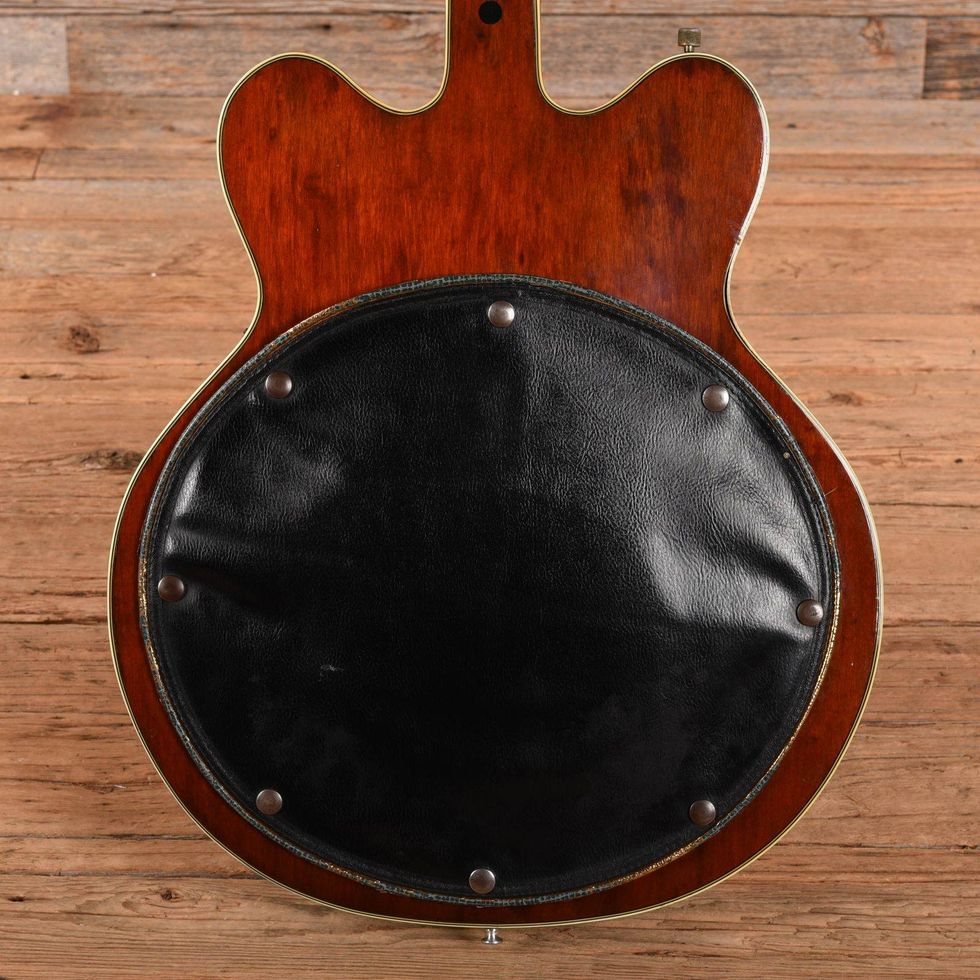 Close-up of the back of a guitar featuring a black round cover and wooden finish.