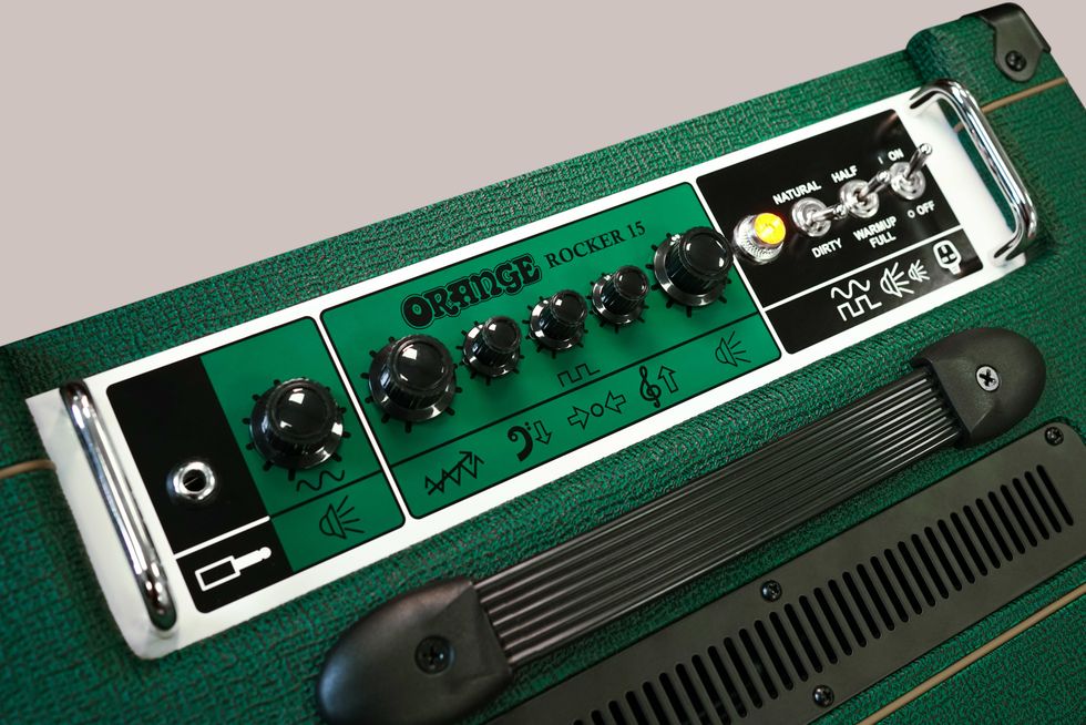 Close-up of the Orange Rocker 15 guitar amplifier controls and knobs on a textured green surface.
