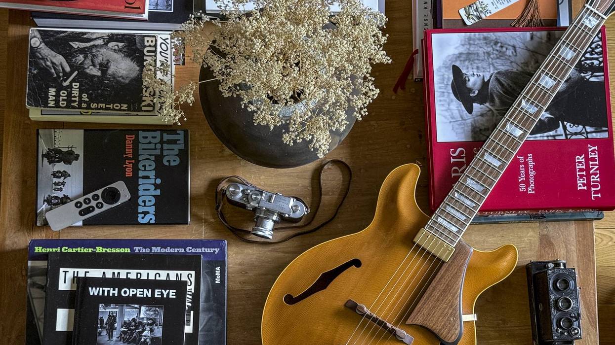 Coffee table scene featuring books, a guitar, cameras, and dried flowers in a vase.