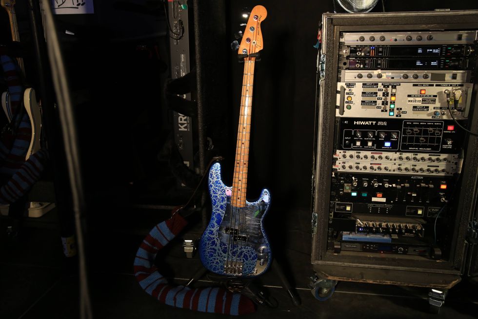 Colorful bass guitar leaning against a rack of audio equipment in a dimly lit space.