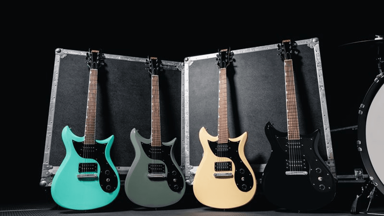 Four electric guitars in various colors lined up against a dark background and cases.