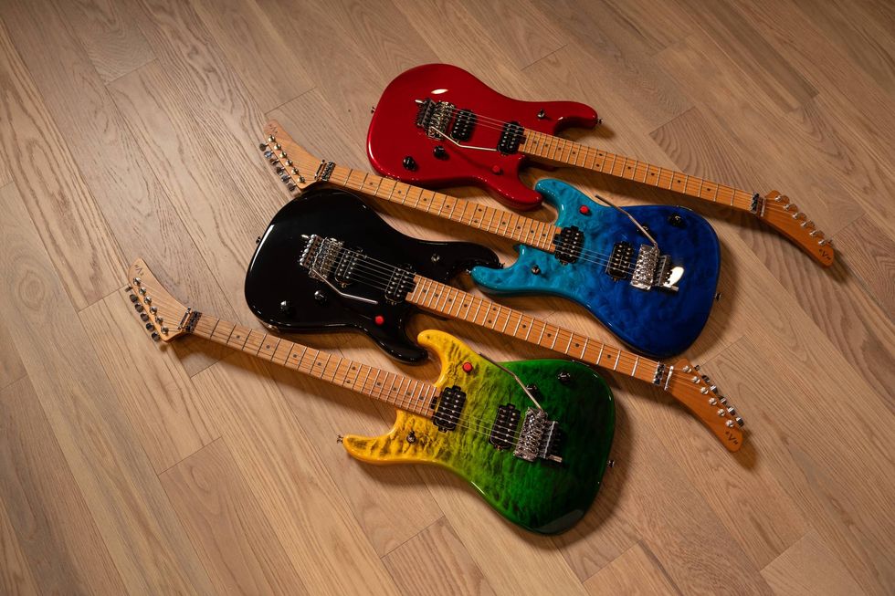 Four electric guitars in vibrant colors\u2014red, black, blue, and green\u2014laid on wooden floor.