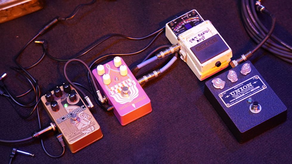 Four guitar effects pedals arranged on a dark surface, connected by cables.