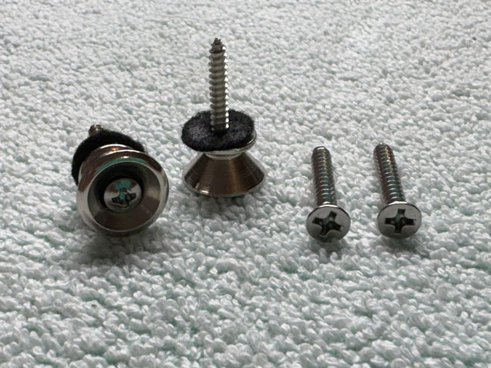 Four metal screws on a textured surface, including two with rubber washers.