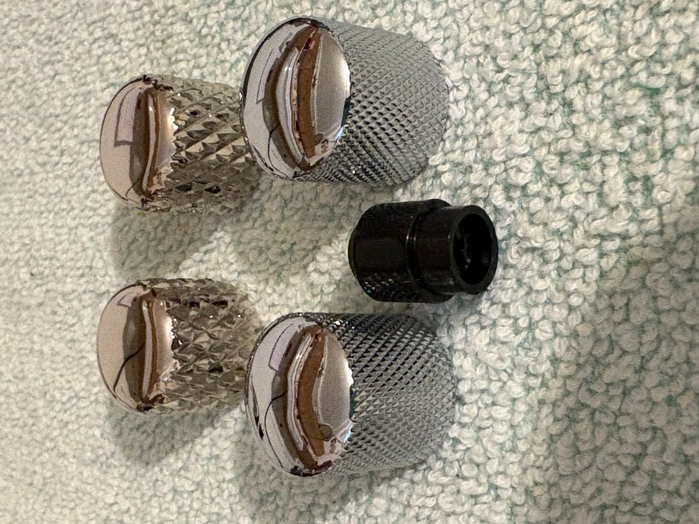 Four metallic screw caps and one black connector on a textured surface.