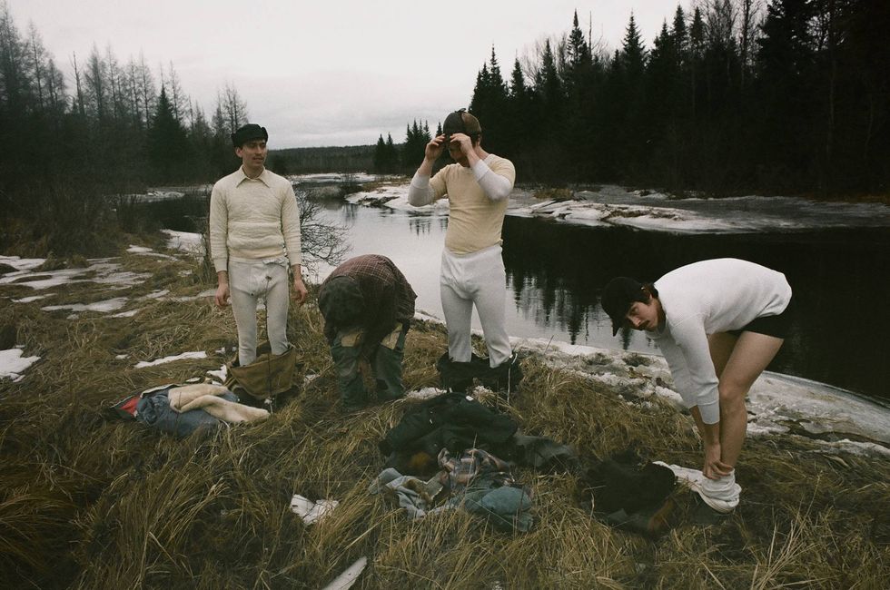 Four people in casual clothing change by a riverbank with trees in the background.