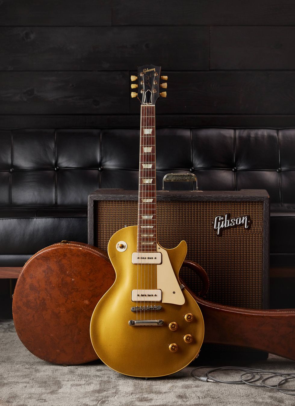 Gibson Les Paul guitar in gold finish, with an amplifier and guitar case on a textured rug.