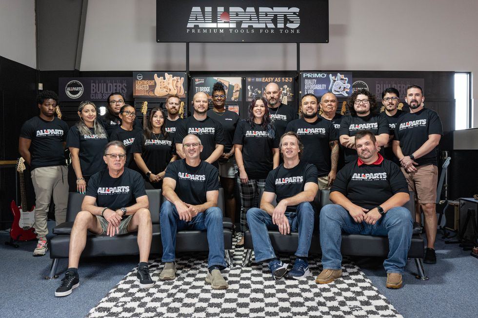 Group photo of All Parts team members wearing branded black shirts in a music store setting.