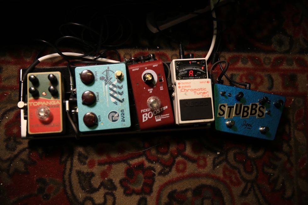 Guitar pedal board featuring various effects pedals on a patterned rug.