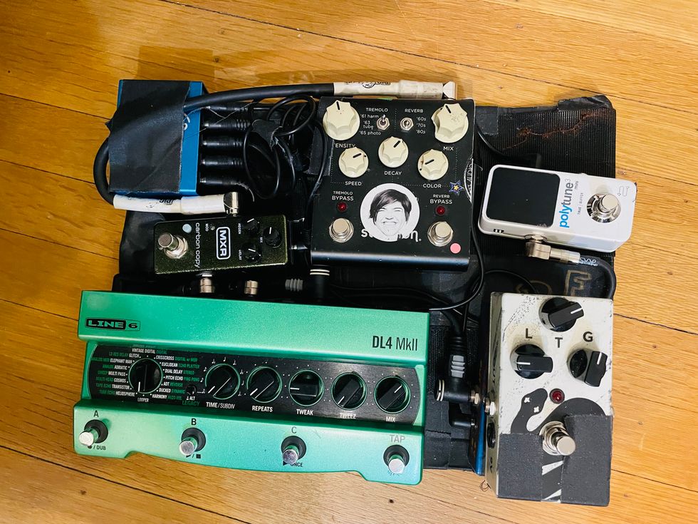 Guitar pedalboard featuring various effects pedals on a wooden floor.