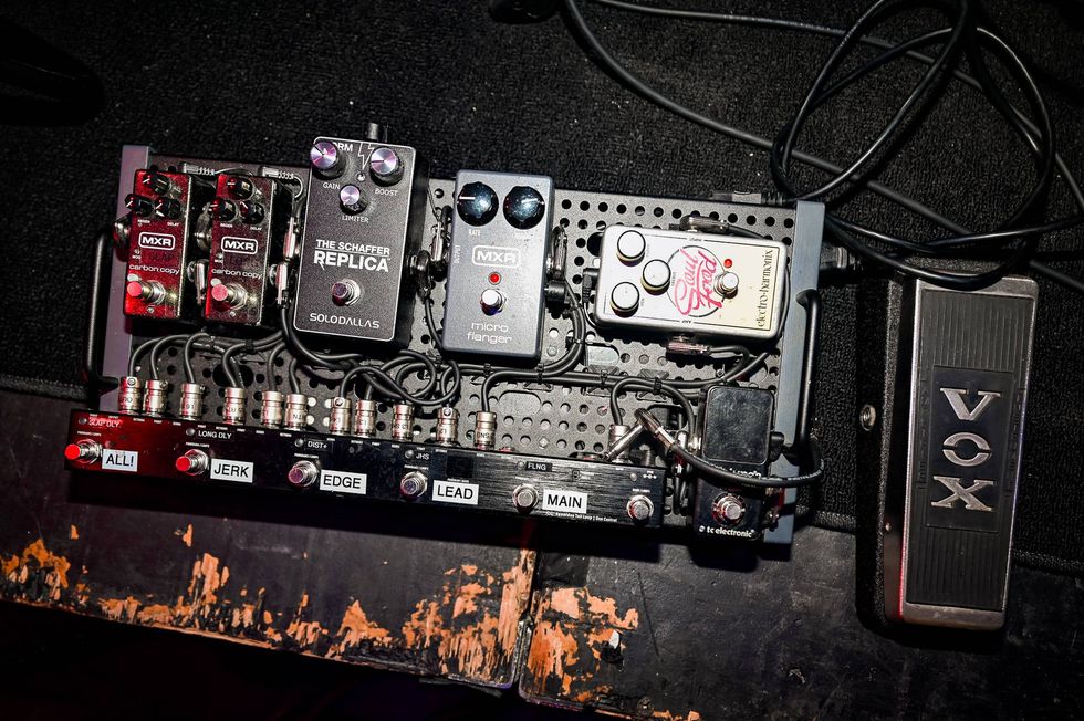 Guitar pedalboard with various effects pedals and a Vox wah pedal on a textured surface.