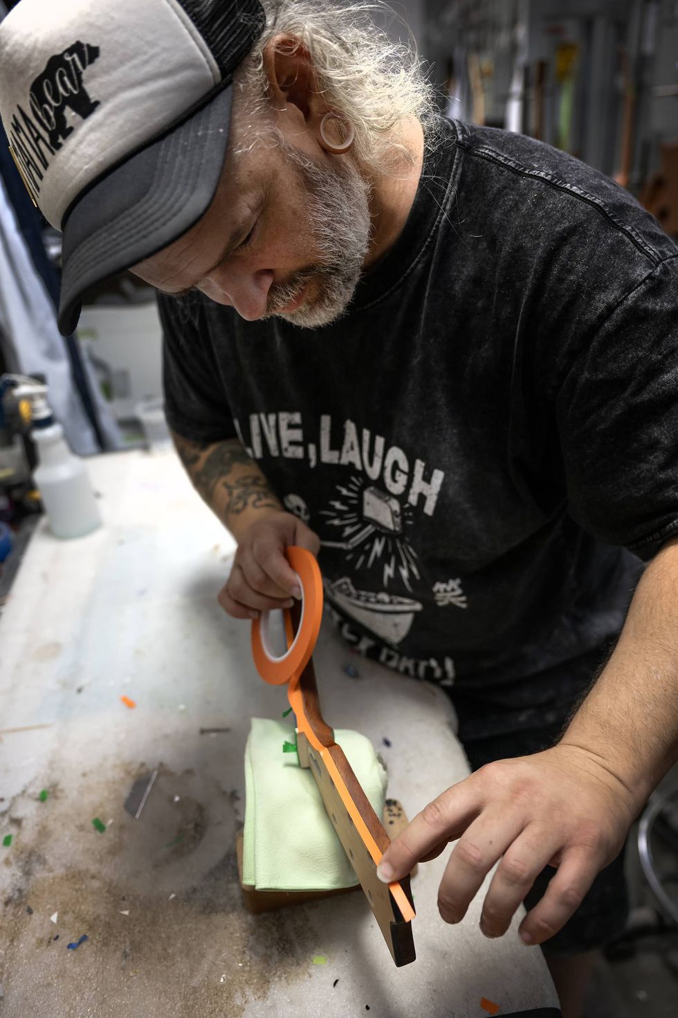 Man focusing on detailing a wooden object using orange masking tape in a workshop.