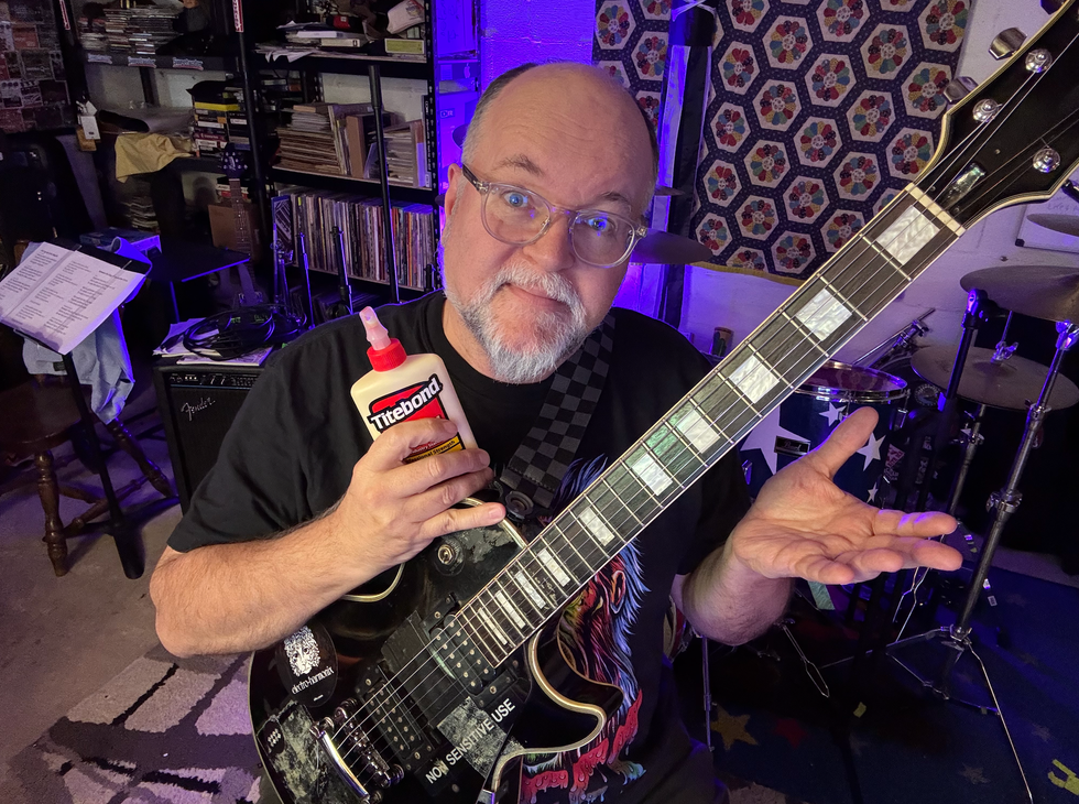 Man holding guitar and wood glue, smiling with a playful gesture in a music studio.